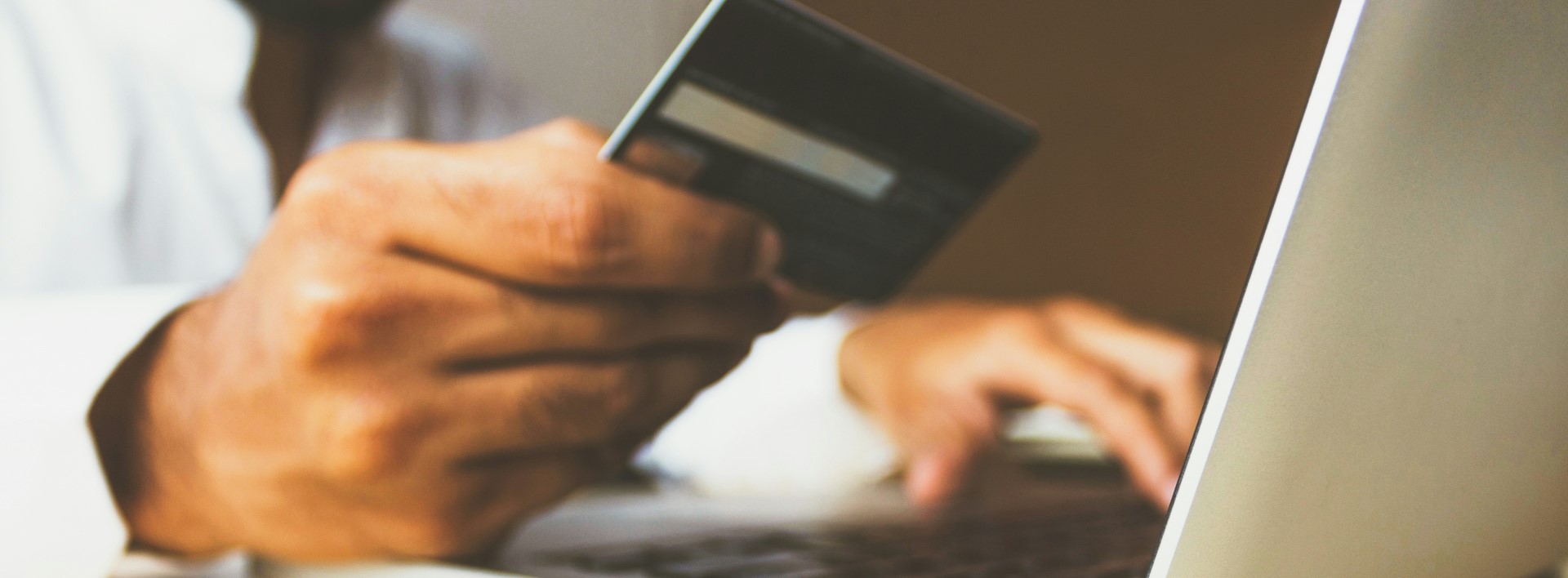 person holding a bank card and typing into a laptop
