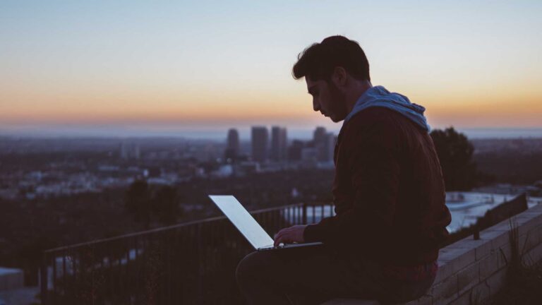 Man on his laptop with an evening skyline