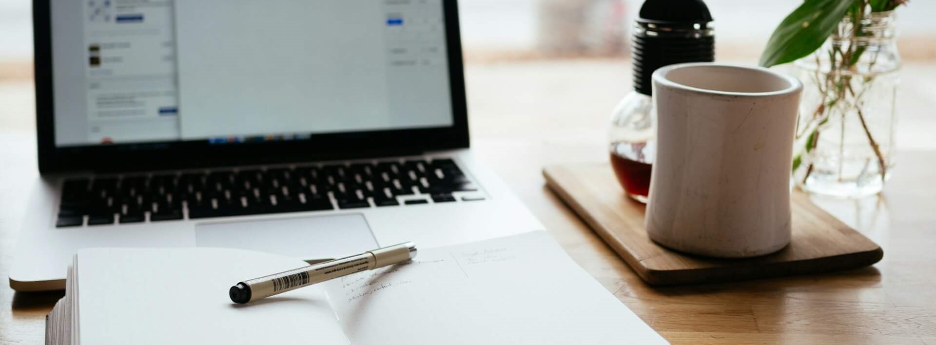 laptop, notepad with pen and coffee mug on a desk