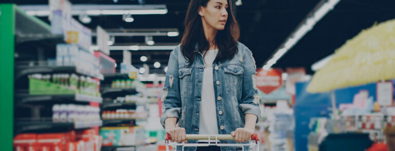Woman pushing a shopping trolley through a supermarket.