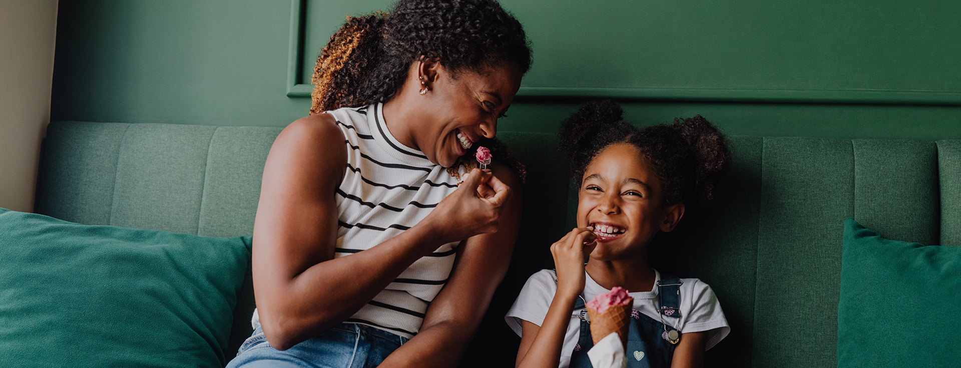 A woman and child are sat on a sofa eating ice cream.