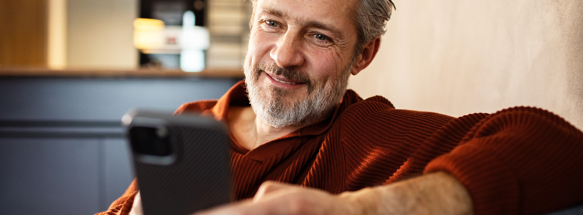 A gentleman with grey hair and beard is looking at a black smartphone.