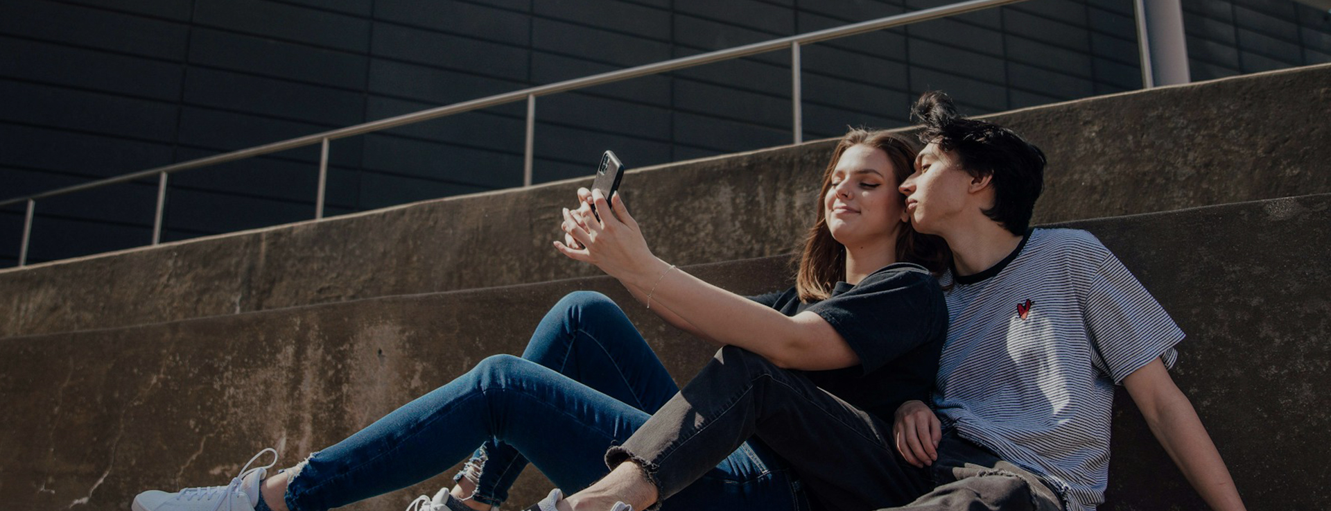 A young man and woman sit on concrete steps to take a selfie.