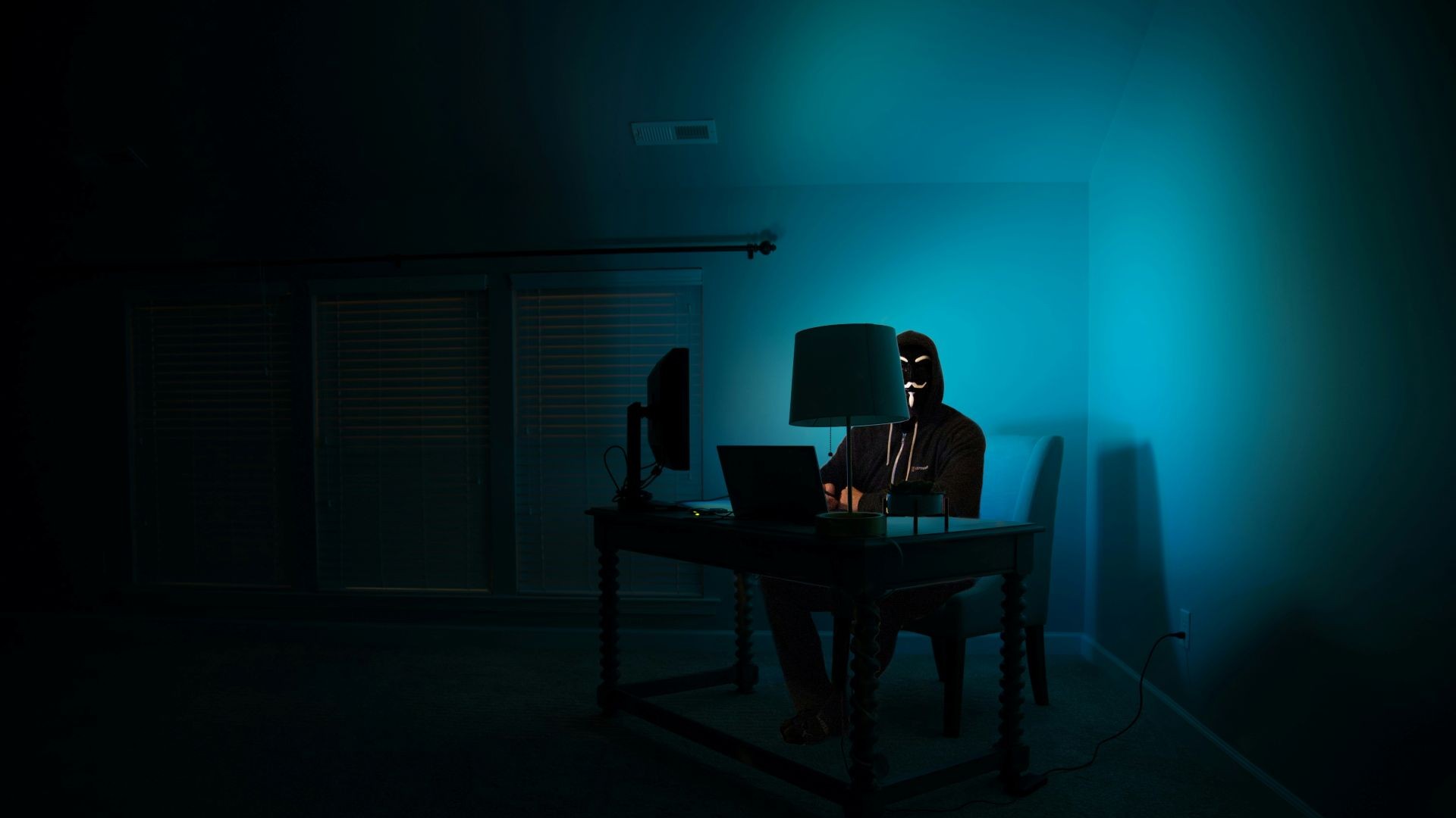 masked figure sits at a computer in the dark