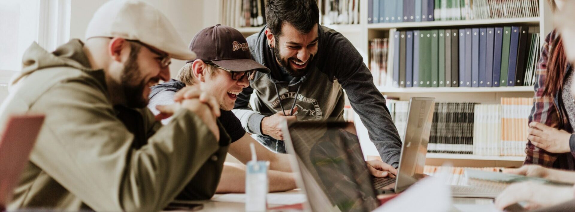 A group of men sit around laptops laughing at the screens